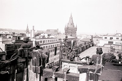 High-angle view from rooftop, Prague, showcasing ornate balustrade & sculptures overlooking cityscape. Visible is Old Town as...