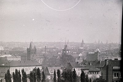 A sweeping cityscape view, likely Prague, featuring numerous church spires and rooftops receding into a hazy distance. Archit...