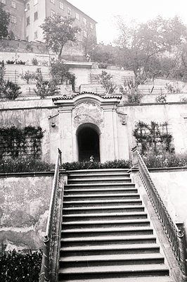 Ornate stone staircase ascends to a monumental entrance framed by a classical archway, flanked by ivy-covered walls. A figure...
