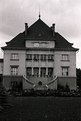 Grand, symmetrical villa with a steeply pitched slate roof & central spire. Three-tiered facade features numerous windows and...