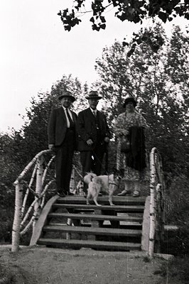 Formal portrait of a family group, including a small dog, on outdoor stone steps with wrought-iron railings. Man in a suit an...