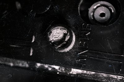 Close-up, monochrome image of a cassette tape mechanism. Shows metal components, including a reel hub and a raised screw. Vis...