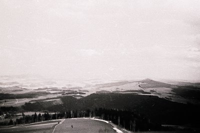 High-angle, panoramic view of a forested valley and rolling hills. Minimal signs of human activity are visible; a road cuts a...