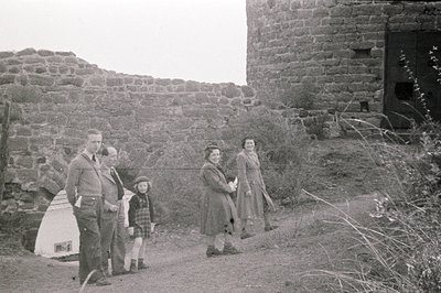 Group portrait: a uniformed man, two children, and two women stand outside a stone building with a heavy wooden door. Likely ...