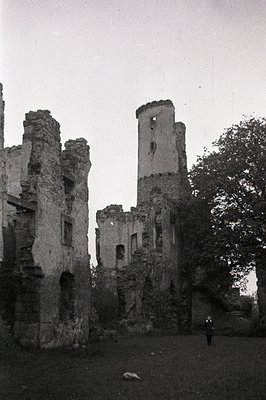 Ruined castle walls rise against a cloudy sky. Crumbling stone architecture shows detailed masonry and remnants of window ope...