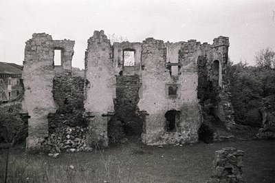 Ruined stone structure with arched window openings and crumbling facade, set within overgrown vegetation. Likely a former res...