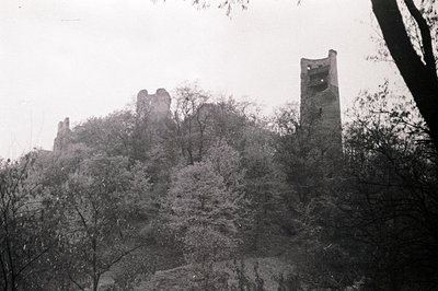 Elevated, partially ruined castle complex on a hilltop, framed by bare trees. A central tower with narrow windows rises above...