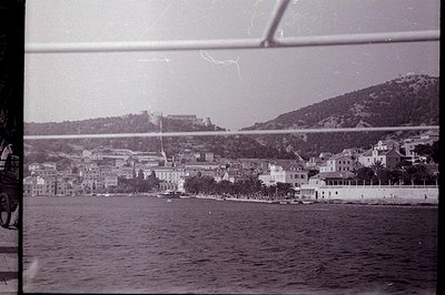 Seaside townscape with a castle overlooking the bay. Architectural details suggest a Mediterranean style. The view is framed ...