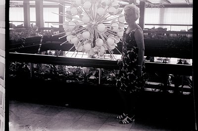 A woman in a floral print dress stands near a large, modern mobile sculpture within a brightly lit, indoor space, likely a ho...