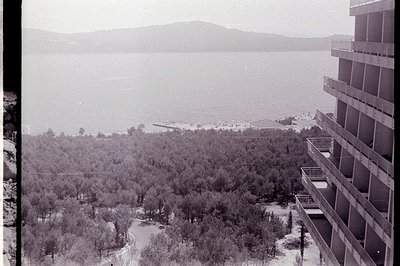 Overlooking a dense, wooded coastline, likely seaside resort. A concrete apartment block dominates the foreground, showcasing...