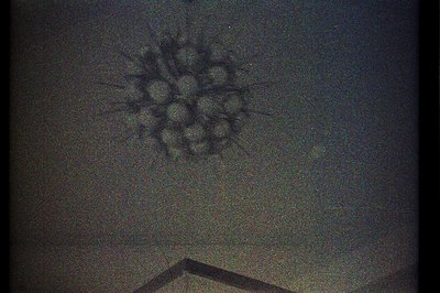 A large, dark chandelier hangs from a ceiling, appearing grainy and blurred. The fixture features multiple, bulbous elements ...