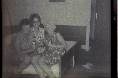 Two women seated on a bench, appearing to be in a public space with architectural detailing visible. The photo exhibits film ...