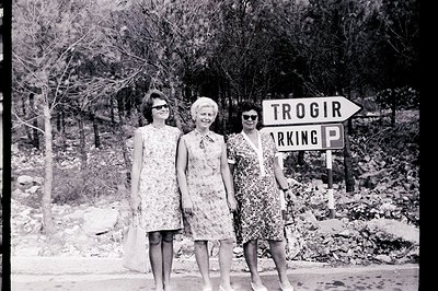 Three women, stylishly dressed in patterned shift dresses, stand next to a “Trogir Parking” sign. Likely Yugoslavia (modern-d...