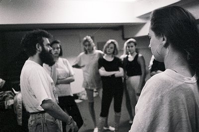 Group portrait, likely a dance class or rehearsal. A man with a beard and casual clothing stands facing a small group of wome...
