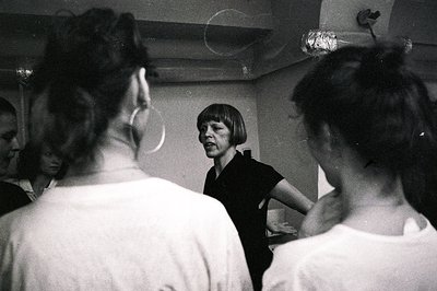 A candid moment: a woman with a short, dark haircut speaks animatedly to a small group. Seen from behind, three figures domin...