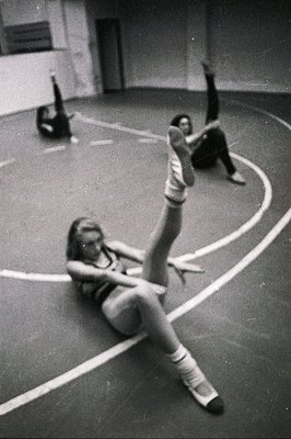 A young woman in sportswear demonstrates gymnastics stretches within a gymnasium, circa 1970s. The linoleum floor’s markings ...