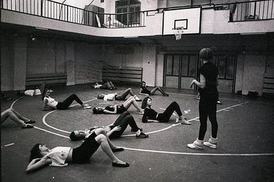 Black & white photo shows a group of young women participating in what appears to be a gymnastics or dance training session w...