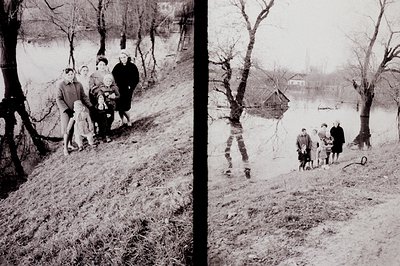 A family group, likely mid-1960s, stands on a grassy bank overlooking a body of water. Several children wear coats, one is ca...