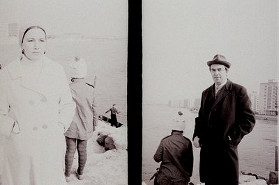 A monochrome, diptych photograph captures a seaside scene. On the left, a woman in a long coat and a child bundled in winter ...