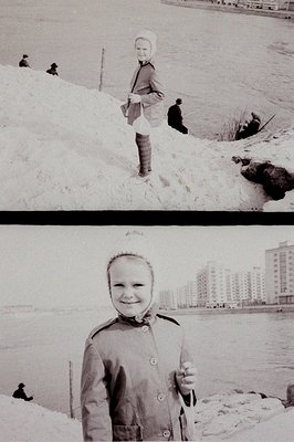 A young child in a winter coat and hat stands on a snow-covered bank, facing the camera. Three other figures are present in t...