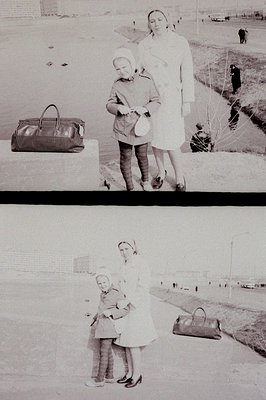 Woman in a long coat stands next to a child, both posed formally. A patterned handbag rests nearby, suggesting travel or a st...