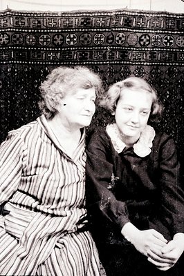 Two women, likely relatives, pose formally, one seated and one standing beside her. The seated woman wears a striped robe; th...