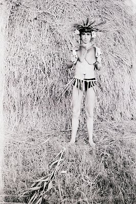 A posed portrait captures a young man adorned in a stylized, possibly ceremonial, costume. He wears a headdress and a necklac...