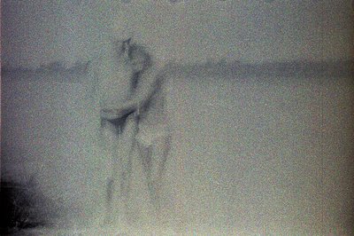 A solitary figure stands on a beach with a blurred ocean backdrop. The subject is facing away from the camera, partially obsc...