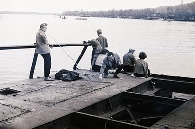 A group of five people are fishing from a weathered concrete pier extending into a large body of water, likely a bay or inlet...