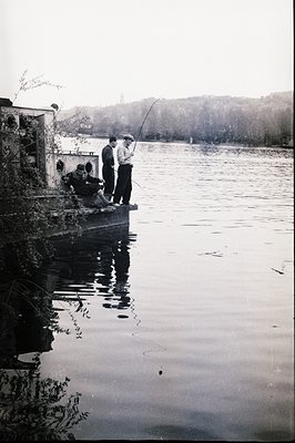 Three men fish from a pier extending into a wide body of water, likely a lake or reservoir. Two men relax on a bench while on...