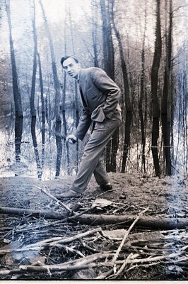A man in a suit strides across a fallen log in a wooded area. The monochrome image shows a stark, possibly Scandinavian, land...
