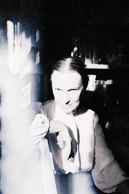 A black and white portrait of a man holding a lit cigarette, appearing mid-motion or blurred. He wears a suit jacket and tie,...