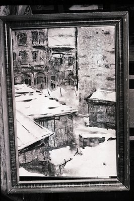 A monochrome photograph depicts a snow-covered courtyard with buildings lining the perimeter. Architectural details show arch...