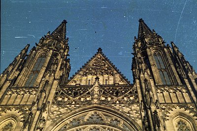 Elaborate Gothic facade with intricate carvings and tall spires dominates the frame against a clear blue sky. Detailed stonew...