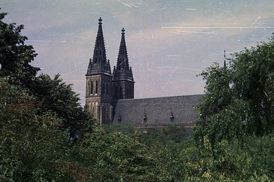 A grand gothic cathedral dominates the view, its twin spires rising against a muted sky. The stone structure displays intrica...
