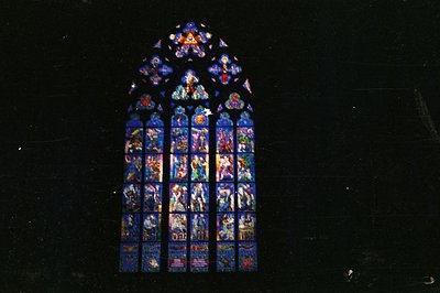 Majestic Gothic window featuring vibrant stained glass depicting biblical scenes and figures. Central image shows a winged fi...