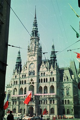The image showcases the striking architecture of a grand municipal building with ornate detailing, spires, and a prominent cl...