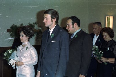 A formal portrait captures a wedding scene, featuring a young couple and two older individuals. The bride wears a shimmering ...
