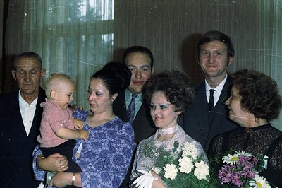 Family portrait, likely a wedding or special occasion. A baby held by a woman in a patterned dress; flanked by three men in s...