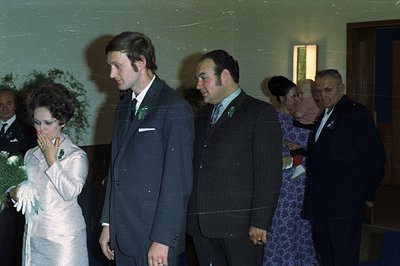 A formal portrait shows a newlywed couple and their families. The bride wears a textured, long-sleeved gown; the groom, a dar...
