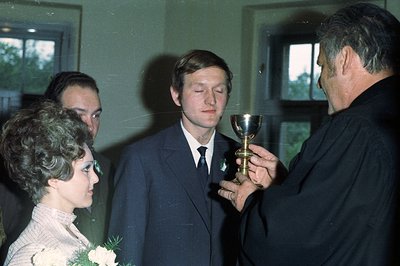 A formally attired man receives communion from a priest during what appears to be a religious ceremony. The man is in a dark ...