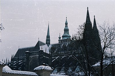 Bleak winter scene showcases a Gothic cathedral with two prominent spires and a central dome. Snow blankets the roof and surr...