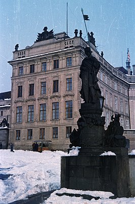 A formal, neoclassical building with a statue in the foreground, likely a governmental or civic structure. Snow covers the gr...