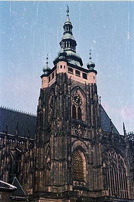High-angle view of a stone gothic tower with clock face. Intricate carvings and pointed arches define the structure's detaile...
