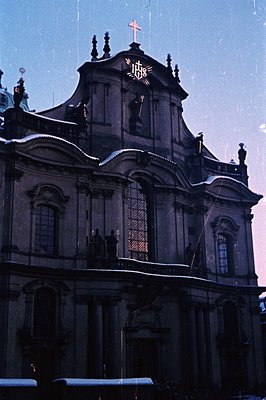 Striking image of a Baroque church facade, partially snow-covered, featuring ornate pilasters and a central, tall window. “JH...