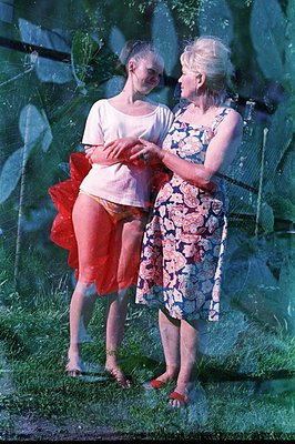 A young woman in a white t-shirt and a red tutu stands next to an older woman in a floral print dress & sandals. Captured out...