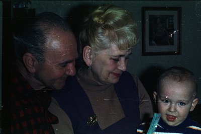 A man, woman, and young child gaze downwards, possibly at a book or object out of frame. The woman has a bouffant hairstyle &...