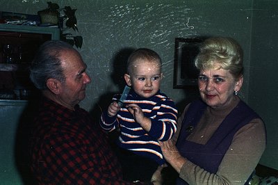A man and woman flank a toddler in this color snapshot. The man wears a red and black checkered shirt; the woman, a purple dr...