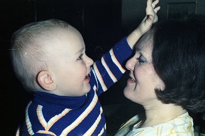 Close-up portrait, likely from the 1970s, shows a young child playfully interacting with an adult. The child, wearing a strip...