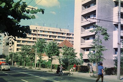 Soviet-era apartment block facade, showing typical brutalist architecture with repeated balconies. Pedestrians cross the stre...